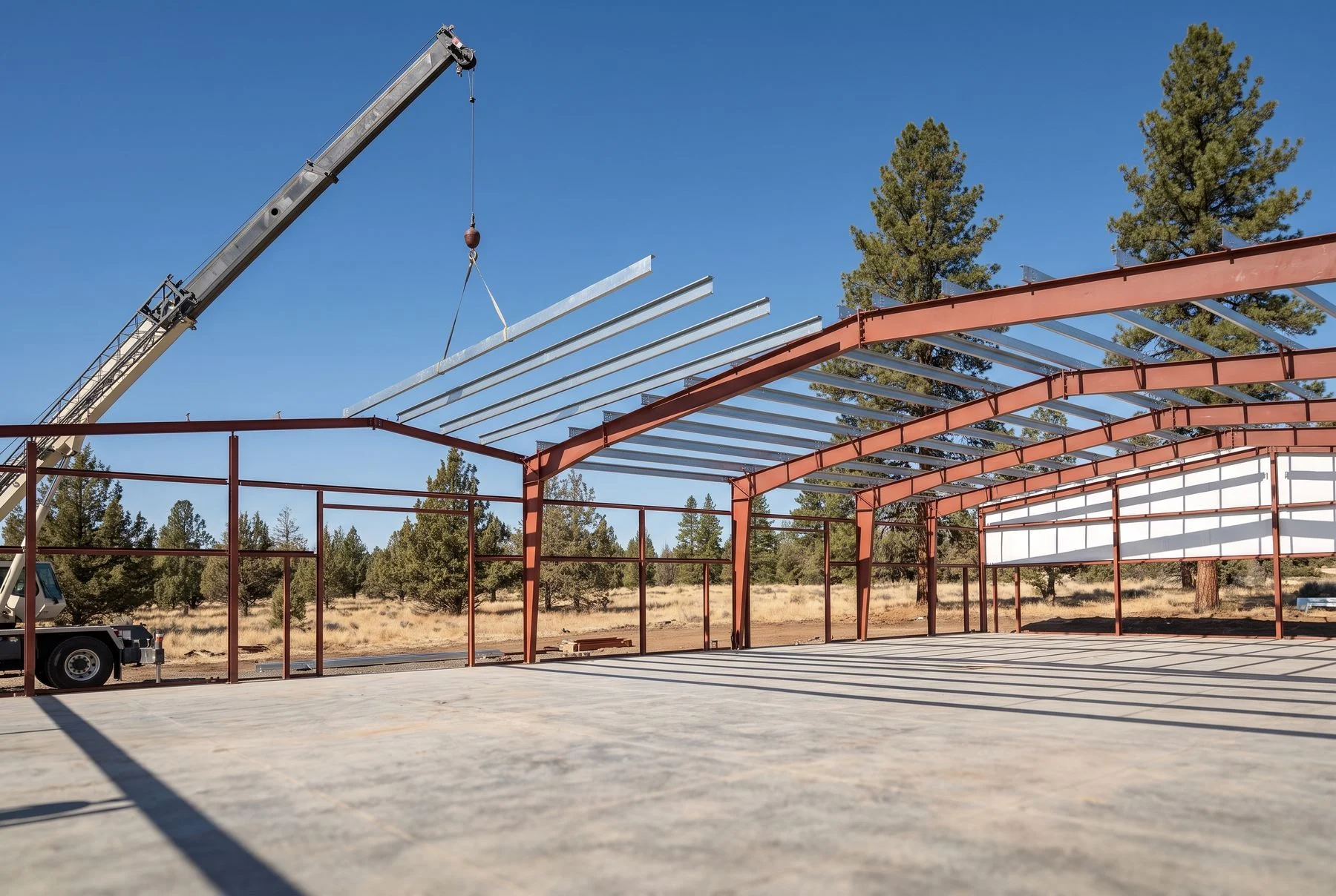 A pre-engineered metal building part way through erection, primed rigid frames standing with purlins going in