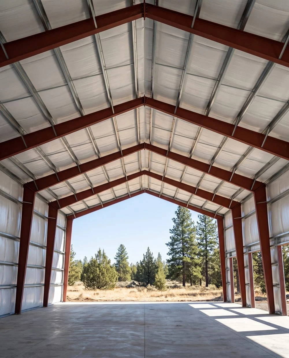 Looking up the ridge of a finished metal building shell, primed frames and purlins running away overhead