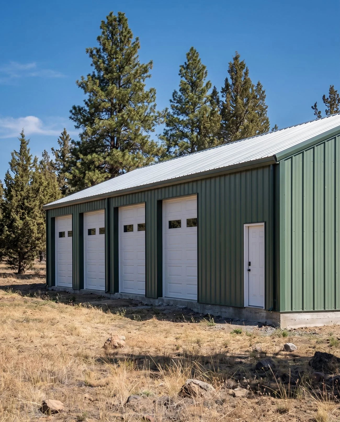 A finished forest green pre-engineered metal building in a Central Oregon pine clearing